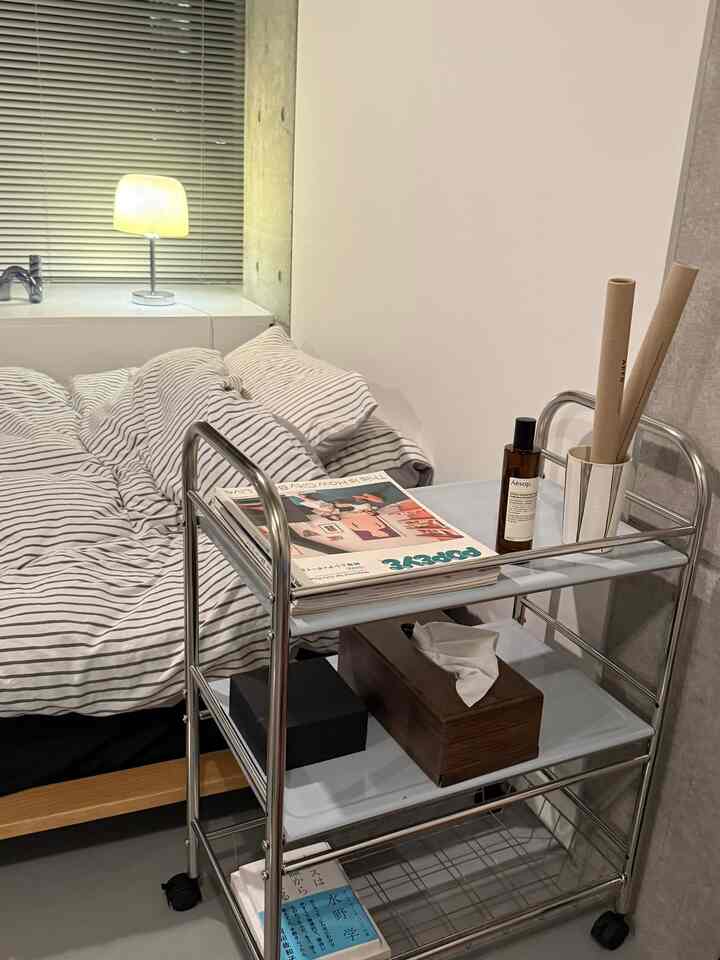 白を基調とした寝室、シルバーのステンレス製3段トロリーカートとストライプ柄の寝具が配されたモダンなインテリア