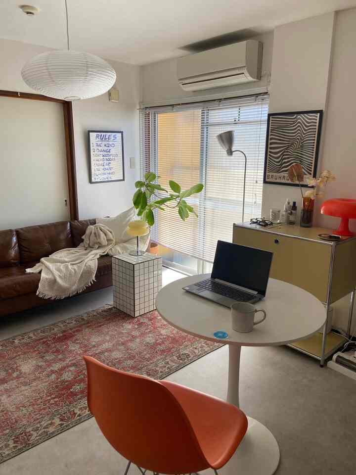 ホワイトとブラウンのトーンが特徴の1DKリビング、ヴィンテージ家具とオレンジ色の椅子が配置された落ち着いた在宅勤務空間