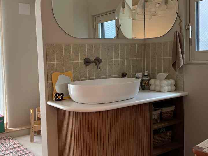 ナチュラルなトーンのベージュ色の壁と木製キャビネットが調和するバスルーム、楕円形の洗面台と大きな鏡が配置された雰囲気のある空間