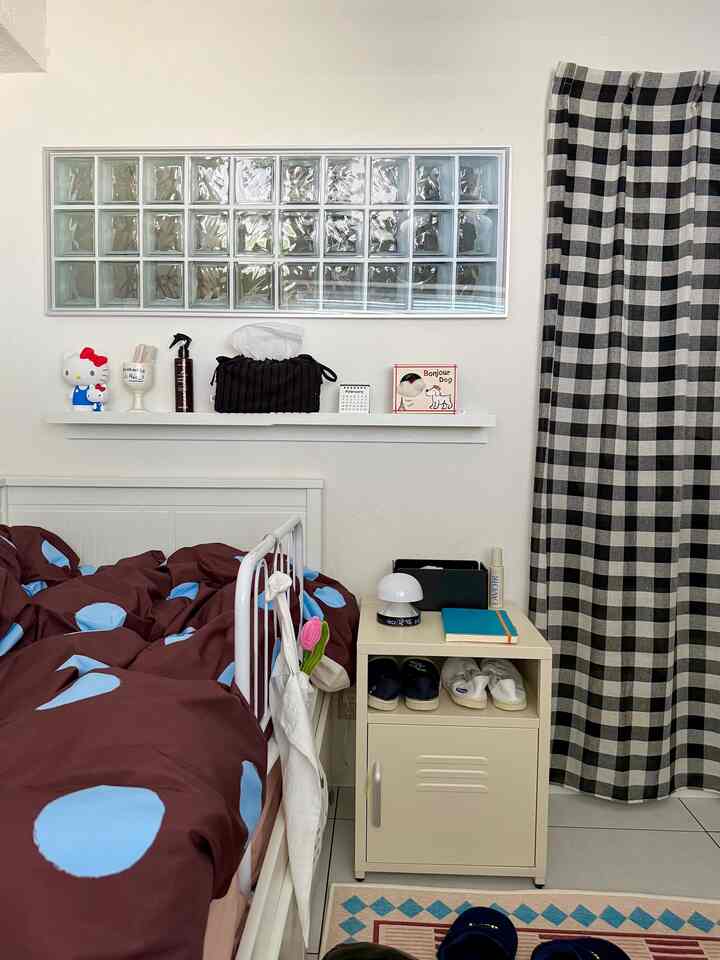 白い壁とナイトテーブル、茶色と水色のドット柄の掛け布団がある狭い寝室のインテリア