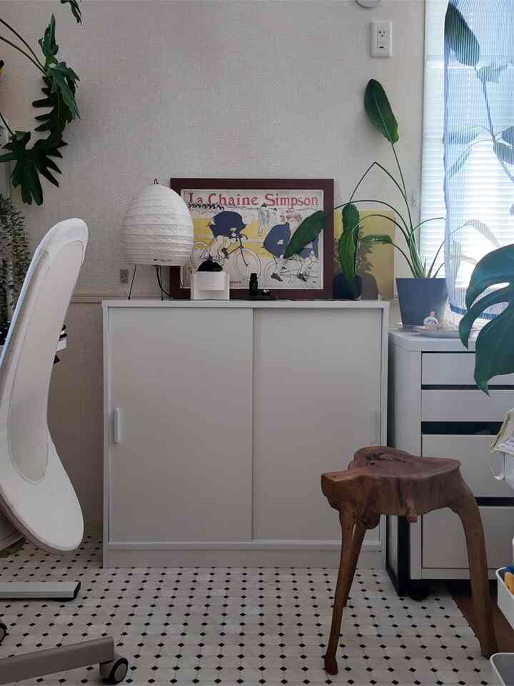 ホワイトとウッドトーンのスタジオアパートメント、シンプルな収納スペースに植物とオフィスチェアが配置された抜け感のあるインテリア