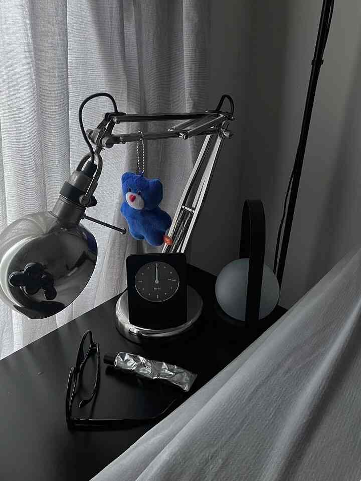 Bedroom nightstand space featuring a silver table lamp, black nightstand, and light gray curtains
