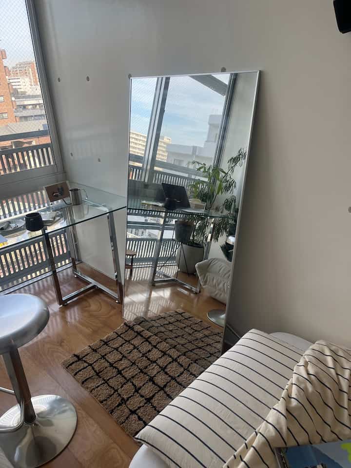 Nordic style living room with natural wood tones and white walls, featuring large full-length mirror, glass table, and bar stools creating a cozy atmosphere