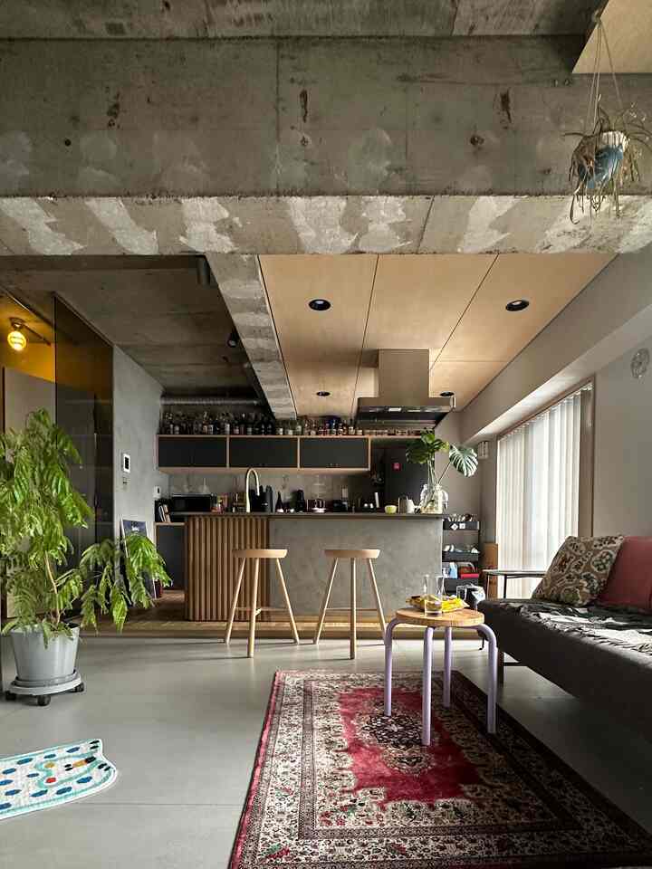 ナチュラルな木調と打ちっ放しコンクリートが調和したモダンなリビングとオープンキッチン、植物が空間に生気を与える落ち着いた雰囲気のインテリア。