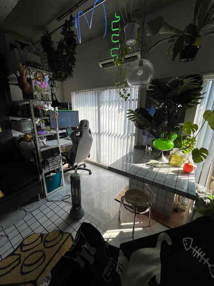 A narrow home office with white and green tones, featuring a gaming chair and lush plants in a modern interior