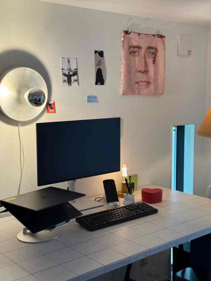 White-toned workspace featuring mid-century modern wall sconce, desk with laptop and monitor neatly arranged