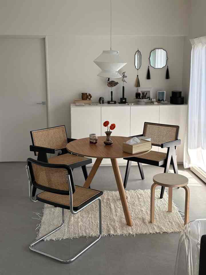 Bright white tone dining room featuring a wooden round table and rattan armchairs with a clean minimal vibe