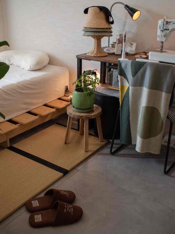 ナチュラルトーンの寝室、木製ベッドフレームとスツール、緑の植物が調和した落ち着いた空間