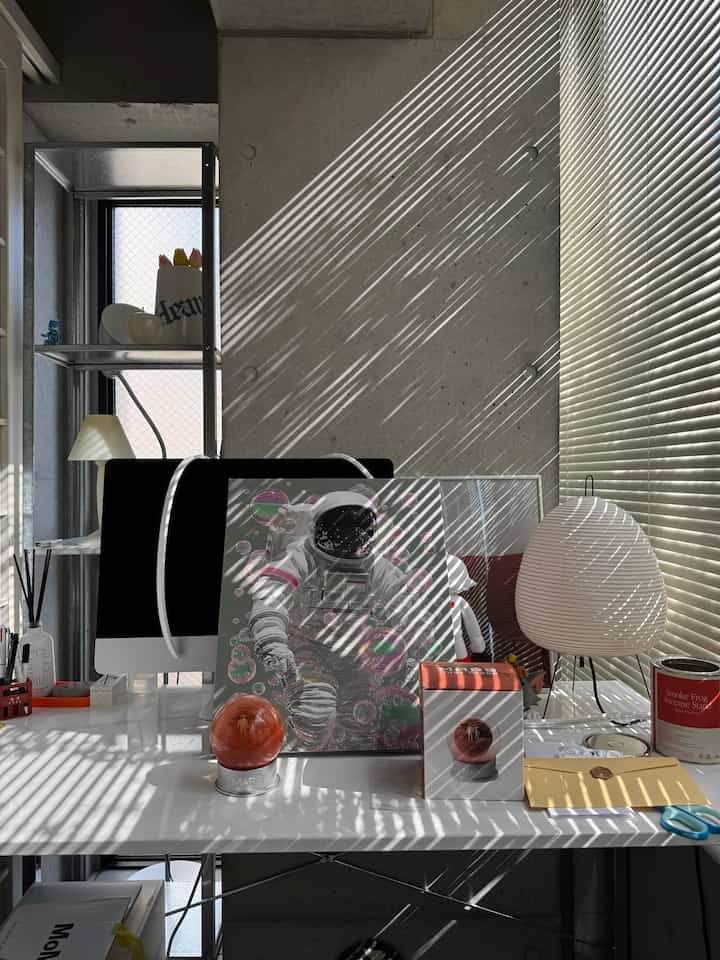 Gray concrete wall and white desk in a Mid-Century Modern styled workspace featuring astronaut artwork and white lighting on desk