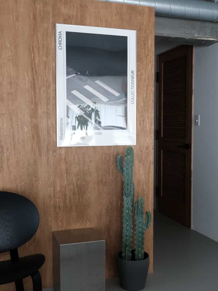 ウッド調の壁と黒い椅子が配置された空間、CHROMAポスターと高さのあるサボテンが調和したモダンなインテリア
