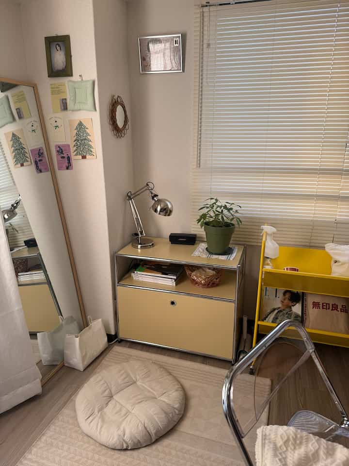 ベージュと黄色のトーンの小さな部屋、シンプルな収納家具と植物、クッションが配置された落ち着いた空間