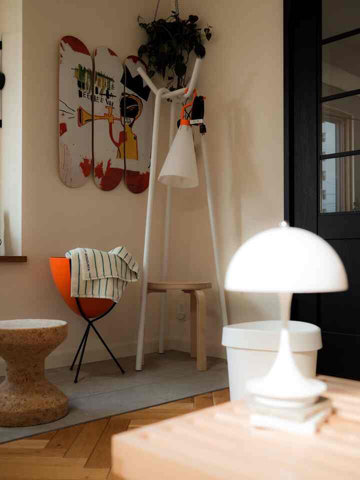 Natural-toned living room corner featuring white coat rack, orange planter, and distinctive lighting elements