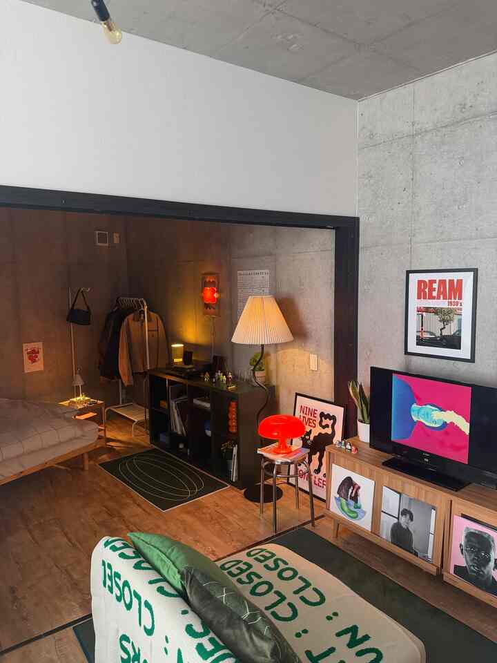 ナチュラルな木目調とグレーのコンクリート壁が印象的なミッドセンチュリーモダンの寝室、ソファとフロアランプ、アートフレームが調和する温かみのある空間