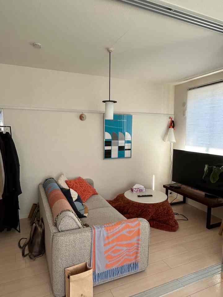 Small living room with natural colors and orange accents, featuring mid-century modern sofa and kotatsu table in a cozy home cinema setup