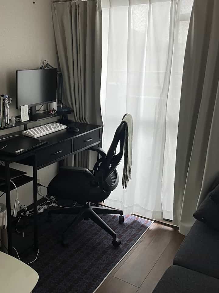 チャコールとベージュの色調のモダンなホームオフィススペース、黒いオフィスデスクとチェアが配置されたリビングの一部