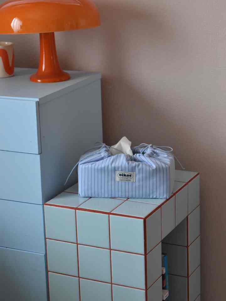 Pastel tone space with blue furniture, featuring an orange lamp and striped tissue case in a simple interior