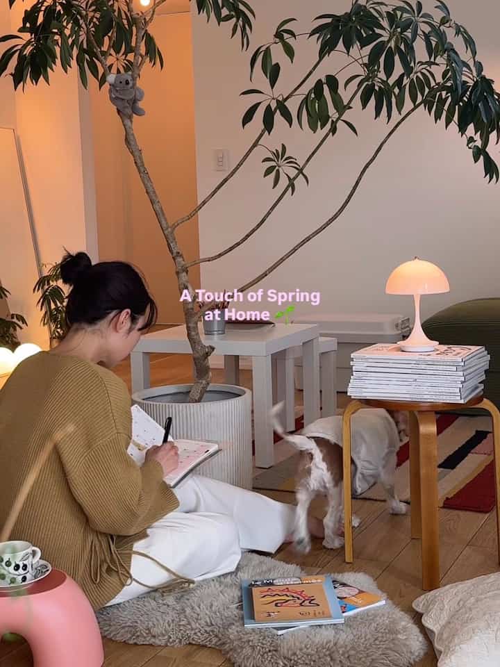 ナチュラルな木製床と大きな植物のある2LDKのリビング、居心地の良い雰囲気で作業し犬と暮らす様子