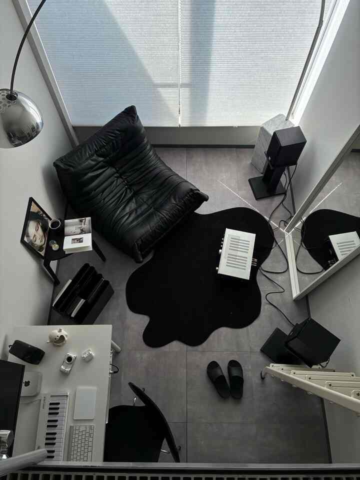 モノトーン調の一人暮らし空間、黒いレザーのアームチェアと大きな鏡、黒いラグが配置された洗練されたモダンな雰囲気のインテリア