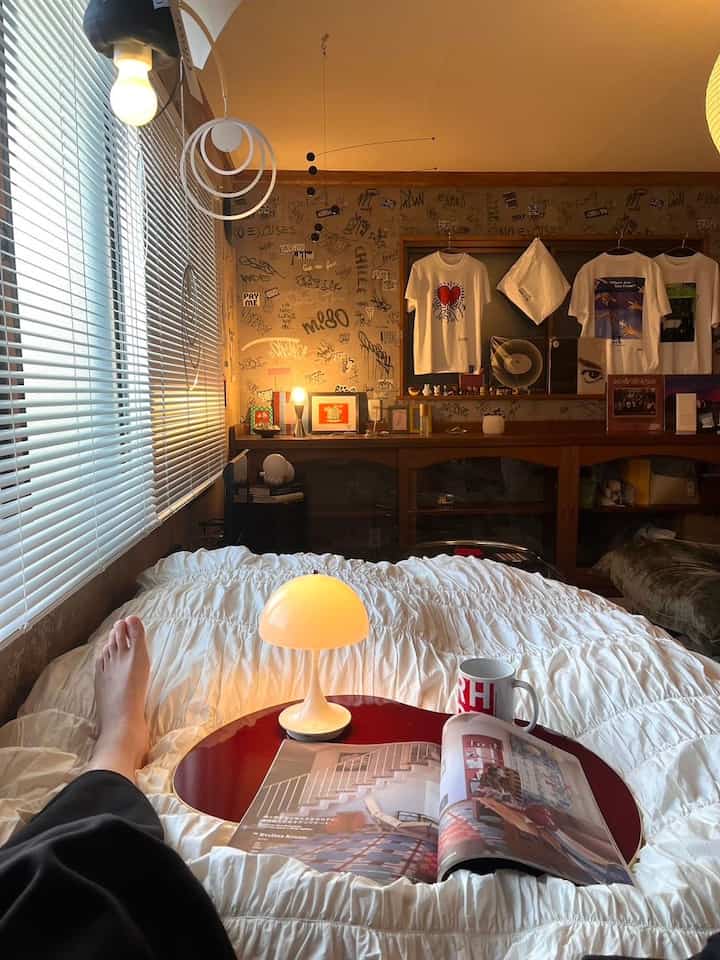 Cozy small bedroom in white and wood tones featuring bed with red tray holding lamp and book