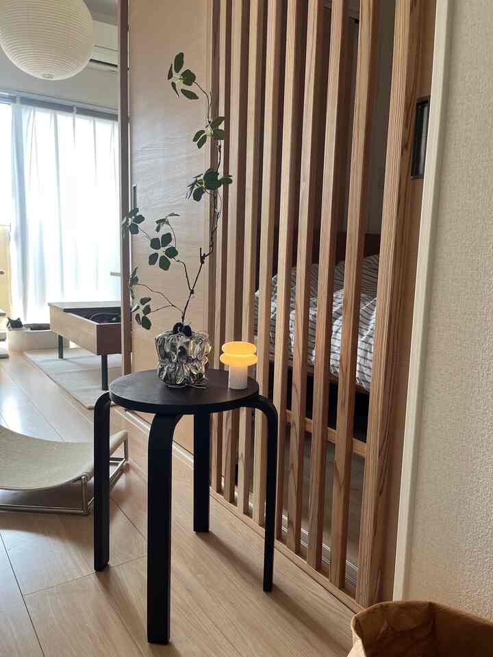 ホワイトとナチュラルな木目調の1LDKリビング、黒いスツールと観葉植物が配置された印象的なモダンな空間