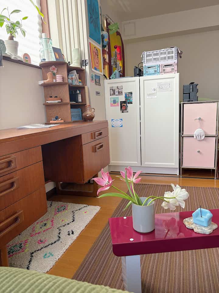 ナチュラルな木目調とピンクのアクセントが調和した居心地の良いワンルームのリビング、机と収納家具が配置された空間