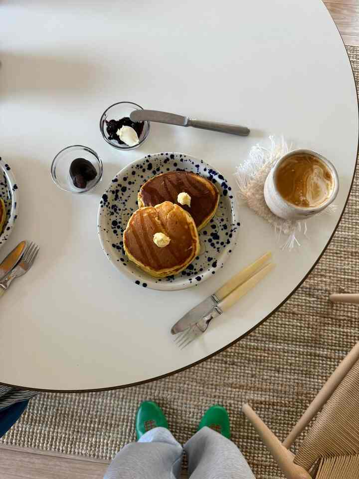 Cozy home cafe setting with a round white coffee table featuring pancakes and coffee, complemented by light wood tones and a beige rug