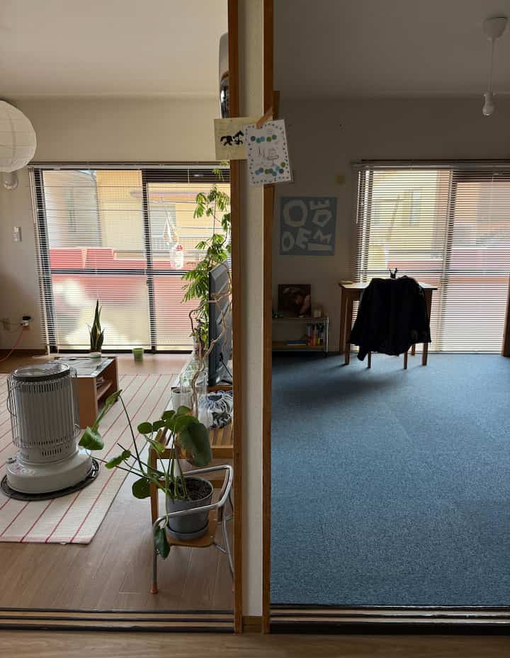 ナチュラルな色調のアパートのリビングとダイニング、広い窓にブラインド、植物が配置された雰囲気のある空間