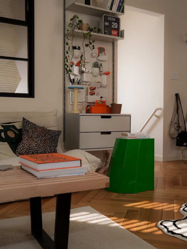 Natural and white-toned compact Mid-Century Modern living room featuring a bench, green stool, wall lighting, and plants in harmony