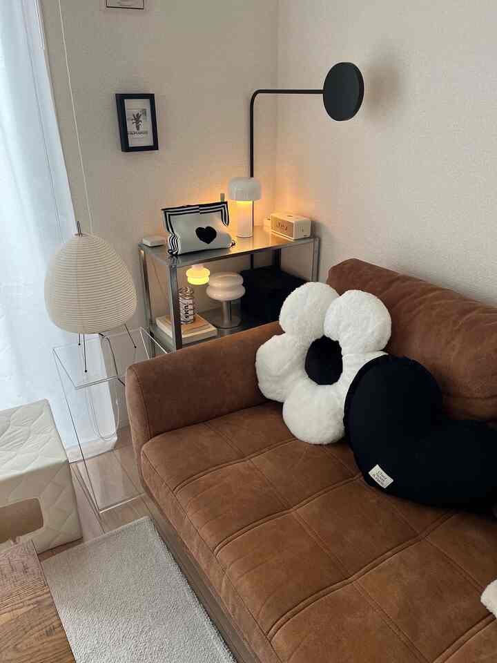 Brown sofa with white flower-shaped cushions in a 1LDK living room, featuring beige pet house and warm lighting for a cozy atmosphere