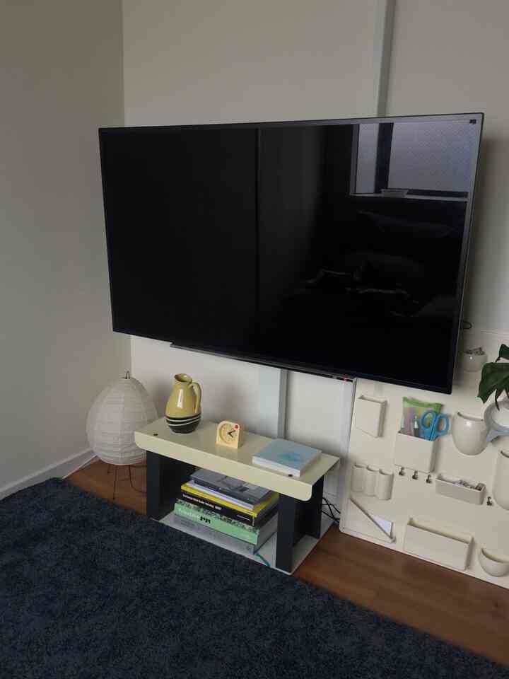 Living room with black TV mounted on central wall, featuring a console table with bookshelf below, creating a neat setting