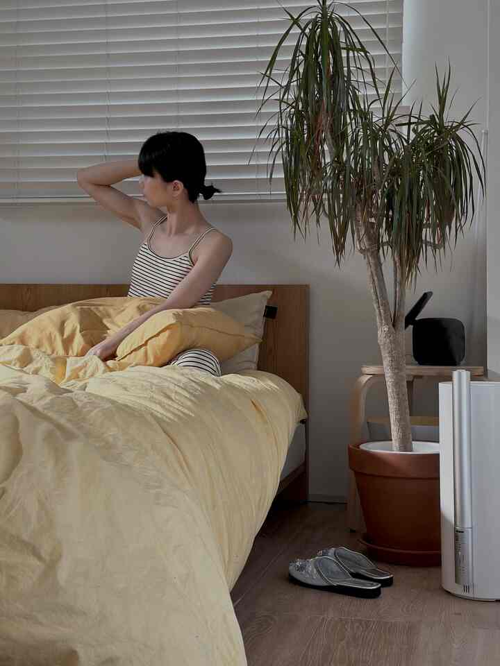 黄色の寝具と木目調家具、植物が配置された温かみのある6畳の寝室、自然でモダンな印象のインテリア