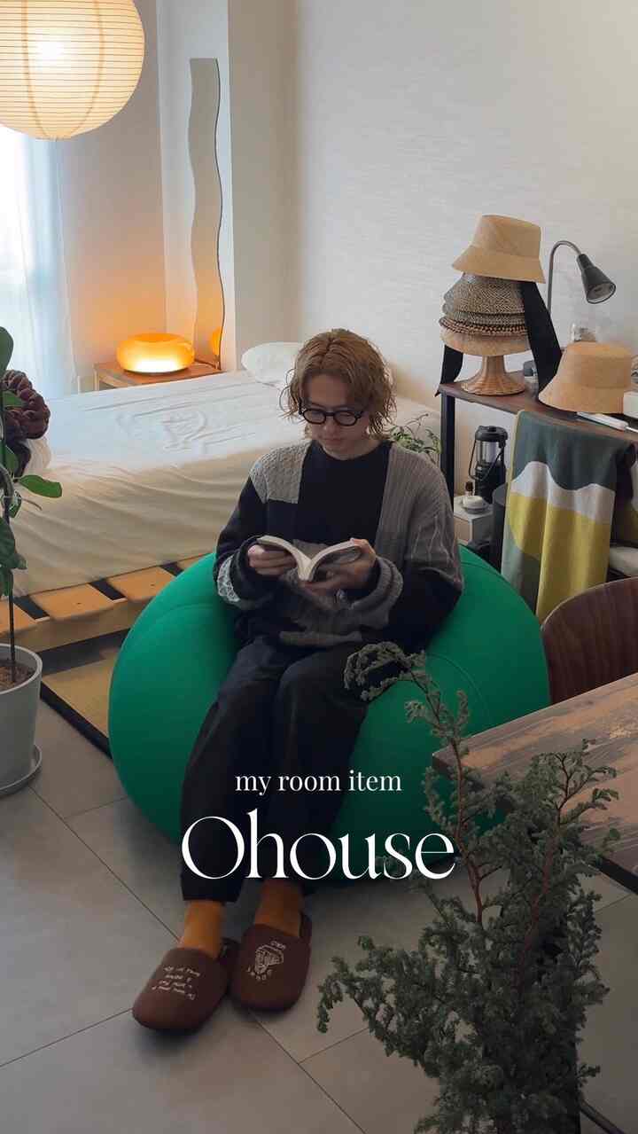 ナチュラルな雰囲気の一人暮らしリビングで、緑のビーズクッションと茶色のスリッパが配置され、本を読む人物がいる印象的な空間