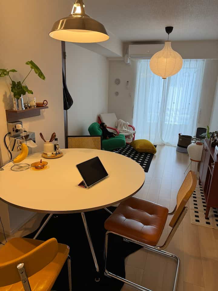 白い壁と黒いラグが配置された一人暮らし用のダイニングルーム、丸いテーブルとナチュラルトーンの椅子が調和する温かみのある空間