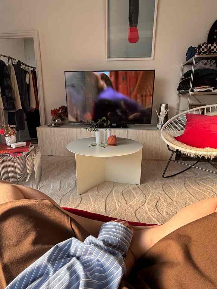 柔らかい白を基調としたリビング、中央に丸いコーヒーテーブルとテレビ台があり、横に赤いクッションの椅子が配置されたミッドセンチュリーモダンのインテリア