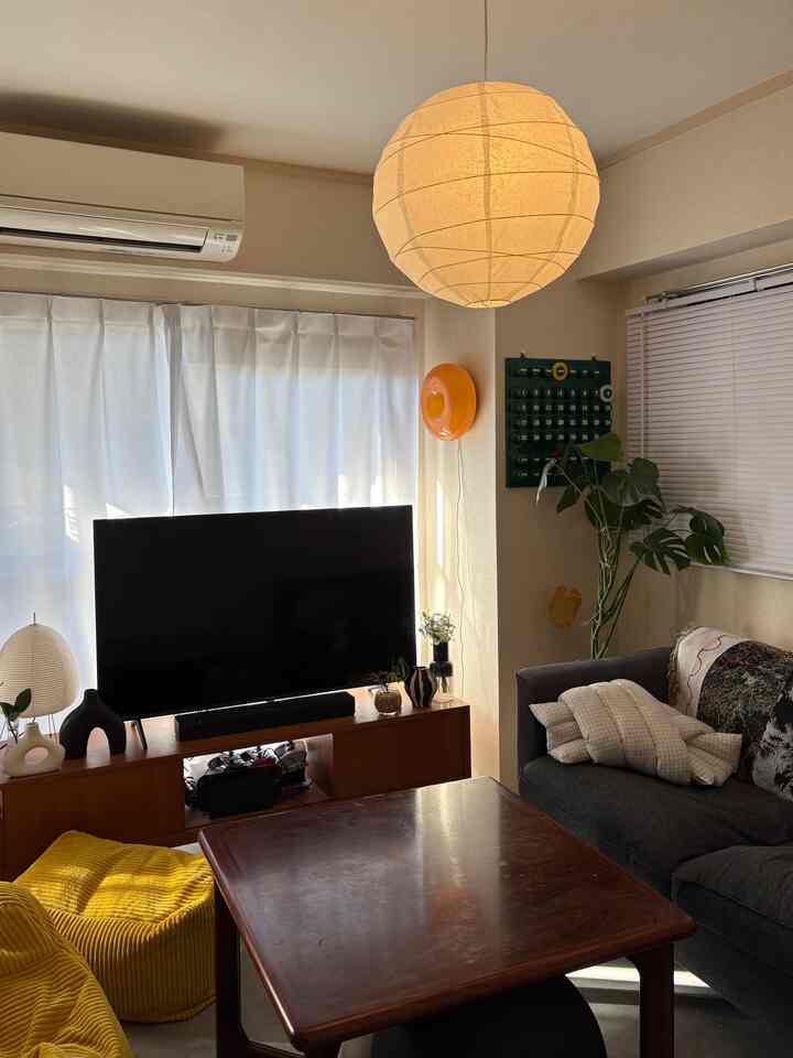 Ivory and brown toned 1LDK living room featuring mid-century modern sofa, lighting, cushions, and a bean bag creating a cozy atmosphere