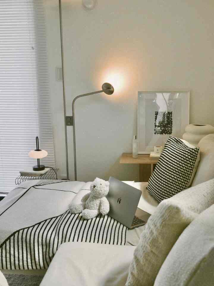 白と木目調の2LDKリビング、ソファとフロアランプ、ぬいぐるみが配置された雰囲気のある空間