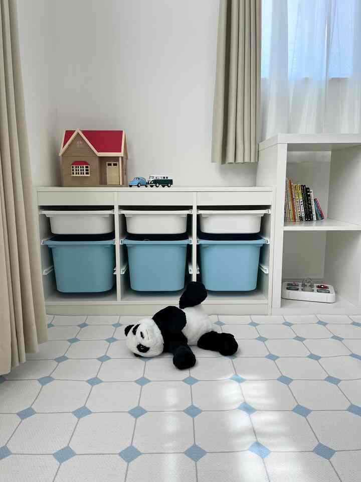A white and blue toned kids' room featuring toy storage cabinets and a neatly arranged floor mat in a simple modern space