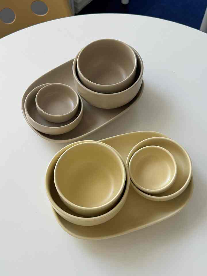 ホワイトの丸テーブルの上に並べられた、2色のベージュの食器セットが配置された印象的なキッチンアイテム