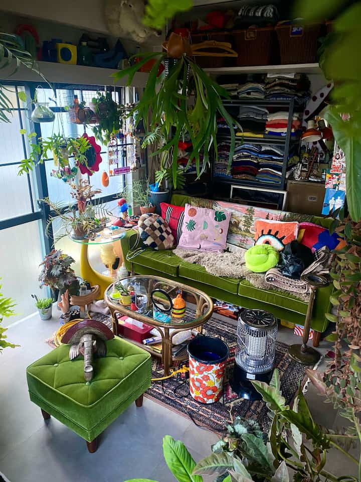 緑色のソファとオットマン、多くの観葉植物が配置されたミッドセンチュリーモダンなリビングインテリア