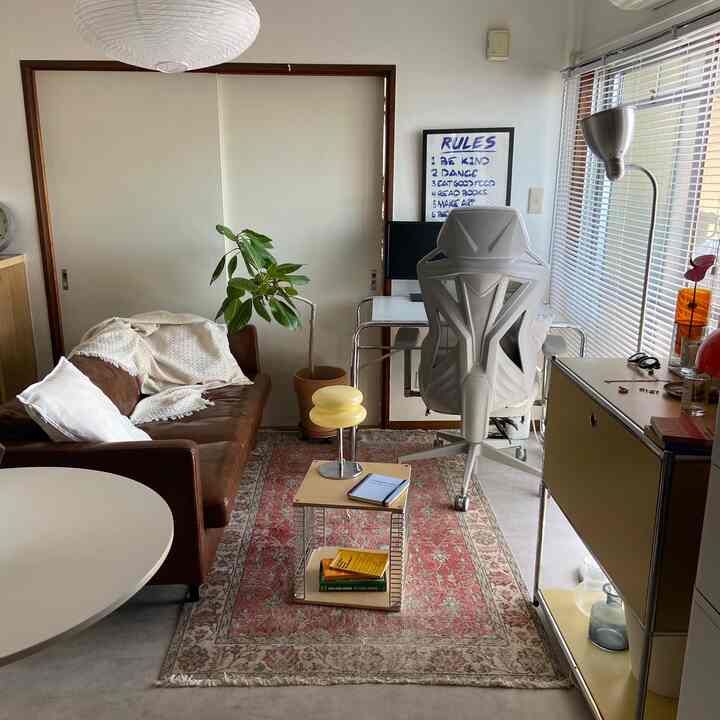 A beige and brown toned 1DK living room combined with home office, featuring mid-century modern furniture and a patterned rug creating a cozy atmosphere