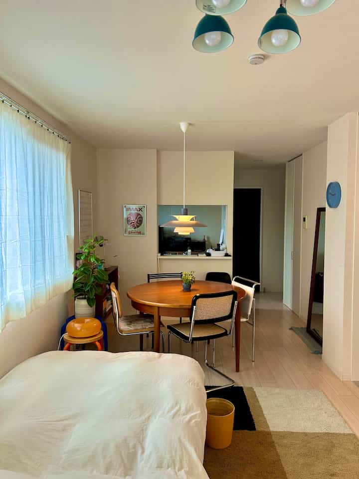 ホワイトとブラウンの色調が特徴の一人暮らし用リビング、ベッドと丸いダイニングテーブルが配置されたナチュラルモダンな空間