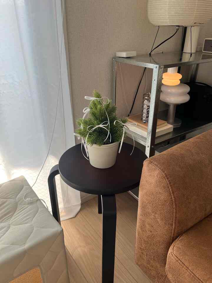 明るく自然な色調の1LDKリビング、黒いスツールと茶色のソファの隣に小さなクリスマス飾りと金属製の棚が配置された雰囲気のあるインテリア