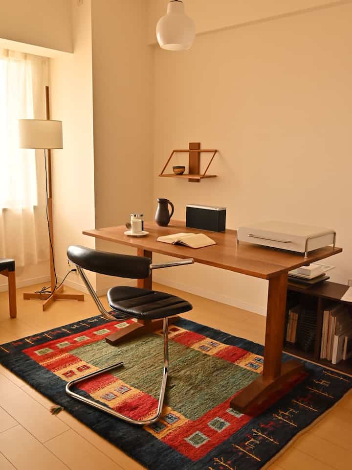 ベージュ色の壁と木目調のデスク、黒いレザー椅子が配置された印象的なワークスペースのインテリア