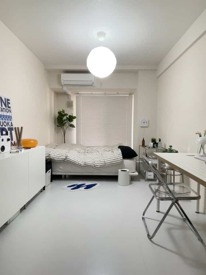 Light gray and white toned compact 1K bedroom for single household, featuring simple furniture and transparent chairs with a clean atmosphere