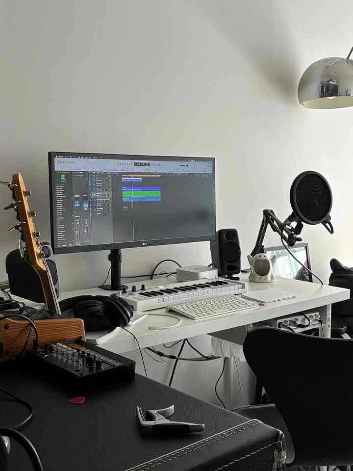 Monotone white and black home office space featuring IKEA desk, audio equipment, microphone, and wide monitor in a sleek workspace