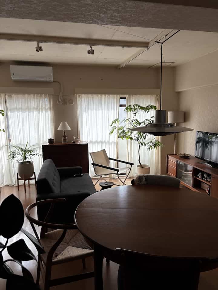 Studio apartment living room in natural wood tones and beige hues, featuring armchair and dining table creating a cozy atmosphere