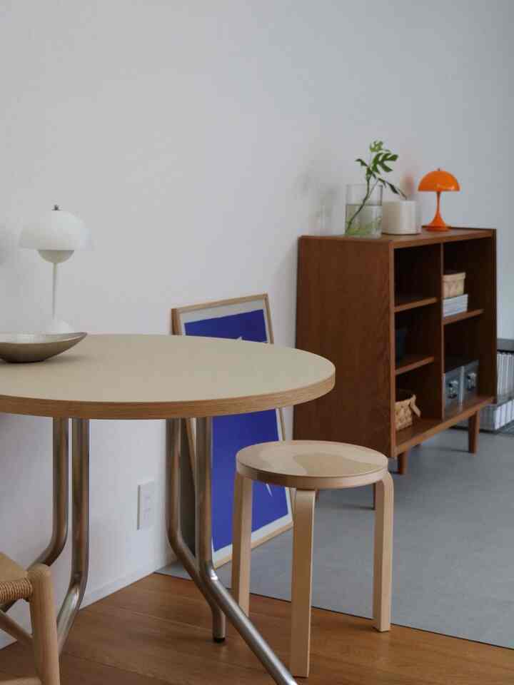 白い壁と茶色の木目調棚が配されたナチュラルモダンのダイニング、テーブルやスツール、照明が置かれたカフェ風の雰囲気あるインテリア