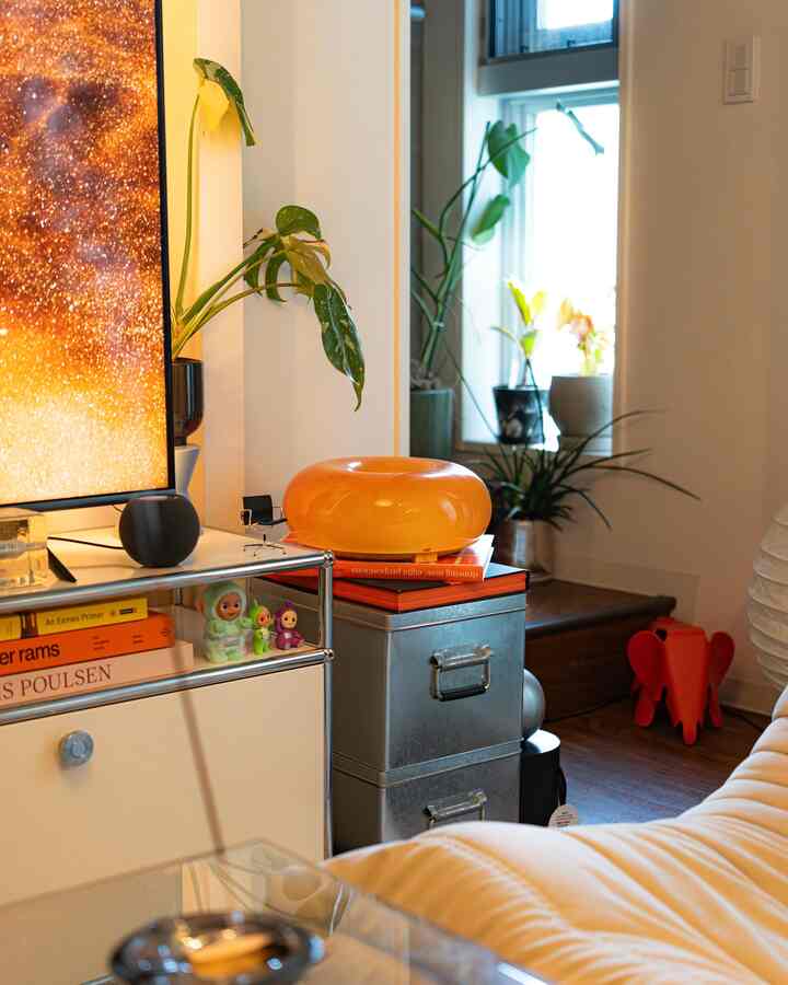 A white and silver-toned living room featuring an orange stool and green plants, showcasing a modern interior design