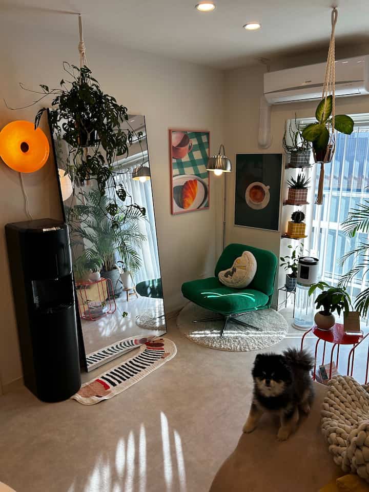 白と緑のトーンのリビング、緑のアームチェアと多様な植物が配置された自然な雰囲気のあるインテリア