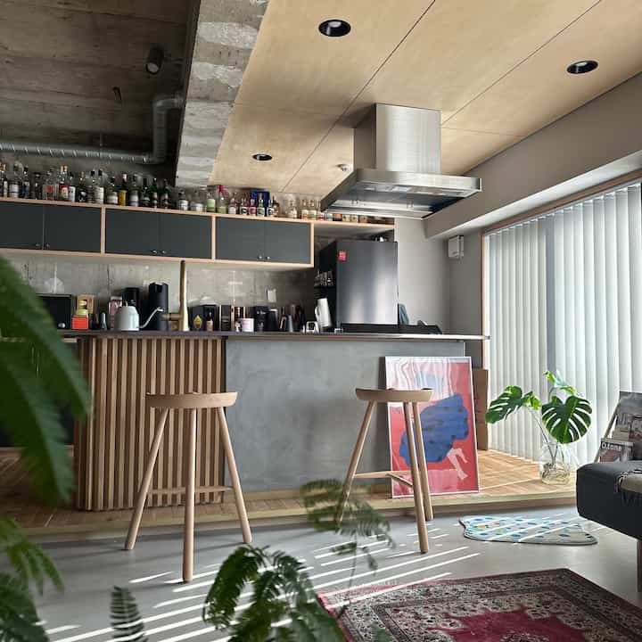 ナチュラルな色調のキッチンとホームバー、バースツールとブラインドが配置された印象的な空間